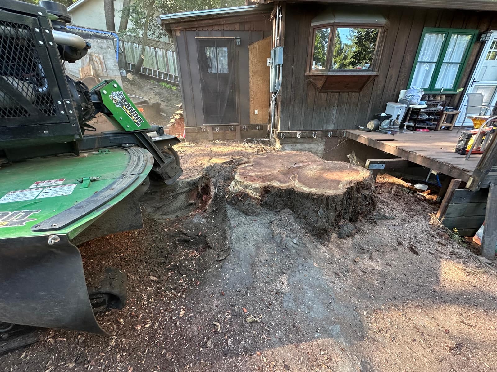 Large stump beside a Bandit SG-40 grinder next to a house deck